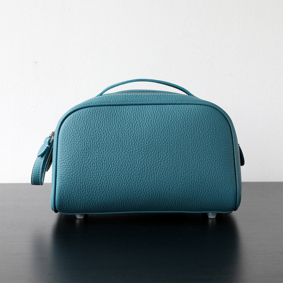 Blue leather makeup bag on a reflective surface with a light gray background